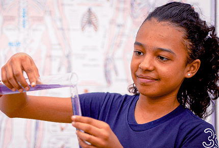 Estudante realizando experimento científico em laboratório escolar, segurando tubos de ensaio com líquido roxo, representando aulas práticas de Ciências no Sistema Etapa.